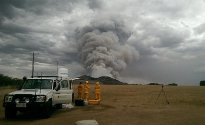 A portable meteorological observation platform, known as the UQ XPOL, making field observations. Image: Atmospheric Observations Research Group, UQ. Firefighters standing near a truck watching a large plume of smoke.